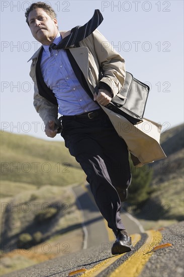 Businessman running on remote road. Photographe : PT Images