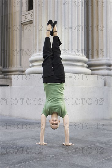 Businesswoman doing handstand on urban sidewalk. Photographe : PT Images