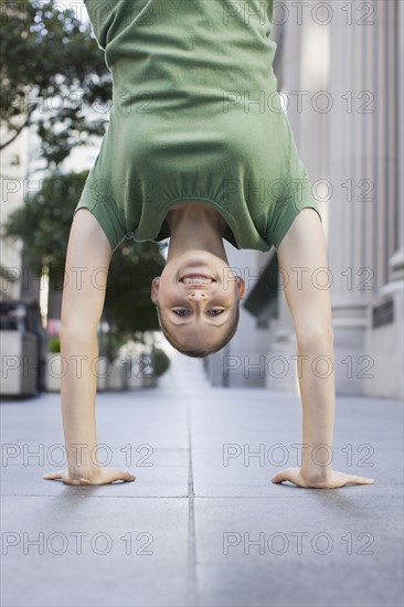 Businesswoman doing handstand on urban sidewalk. Photographe : PT Images