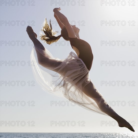 Dancer leaping on beach. Photographe : PT Images