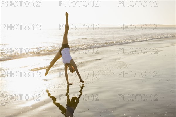 Woman doing cartwheel on beach. Photographe : PT Images