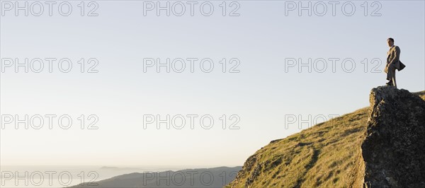 Businessman standing on rock overlooking ocean. Photographe : PT Images