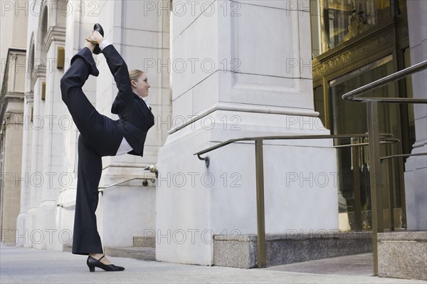 Businesswoman stretching on urban sidewalk. Photographe : PT Images