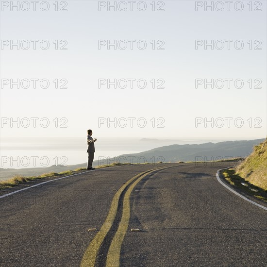 Businessman standing on remote road. Photographe : PT Images