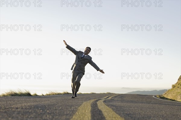 Businessman running on remote road. Photographe : PT Images