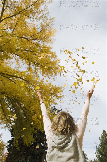 Woman throwing autumn leaves in air.