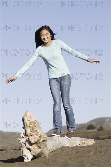 Teenage girl balancing on driftwood. Photographe : PT Images