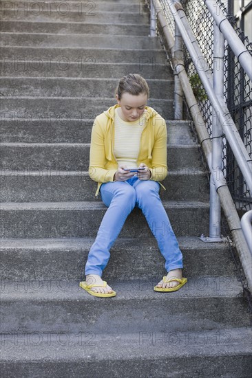 Girl text messaging on steps. Photographe : PT Images