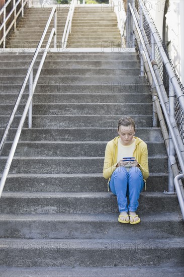 Girl text messaging on steps. Photographe : PT Images