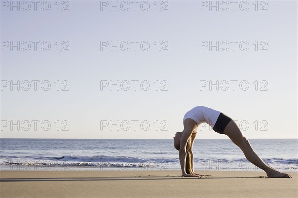 Woman doing yoga on beach. Photographe : PT Images