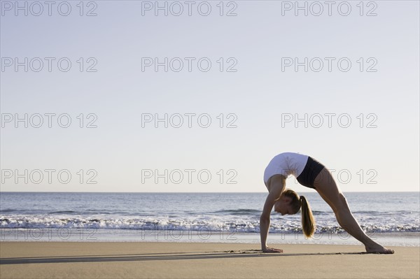 Woman doing yoga on beach. Photographe : PT Images