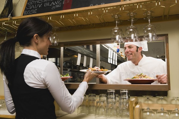 Chef giving waitress plates of food.