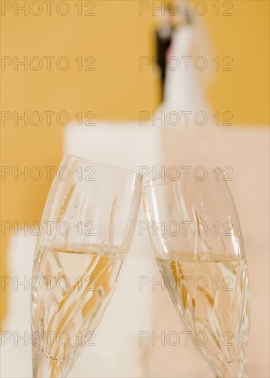 Close up of toasting champagne glasses and wedding cake. Photographe : Jamie Grill
