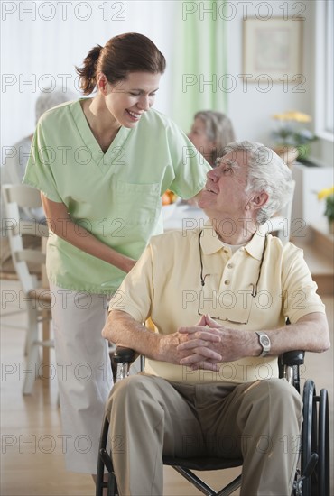 Nurse helping senior man in wheel chair.