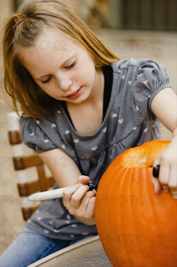 Fillette dessinant sur un potiron pour Halloween