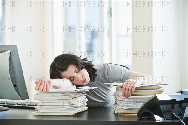 Business woman sleeping on paperwork at desk in office.