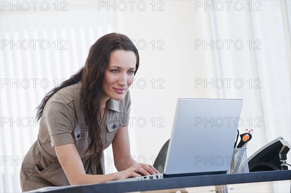 Woman using computer in office, smiling.