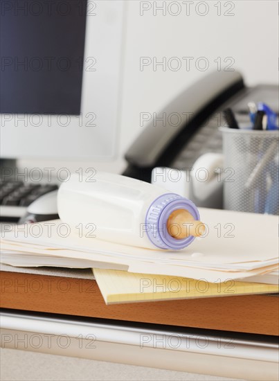 Baby bottle on desk of working mother in office. Photographe : Jamie Grill