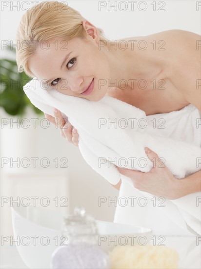 Young woman wrapped in towel and drying face, portrait. Photographe : Jamie Grill