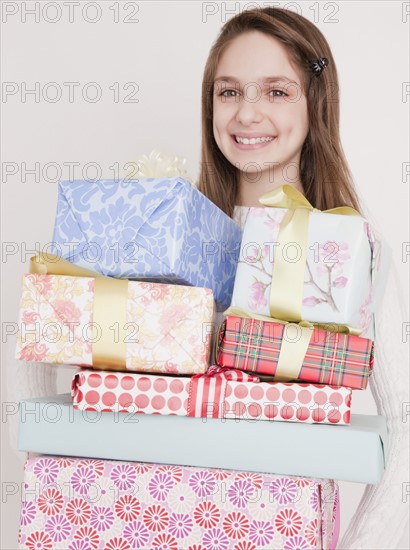 Preteen girl (10-12 years) with stack of birthday presents, smiling, portrait. Photographe : Jamie Grill