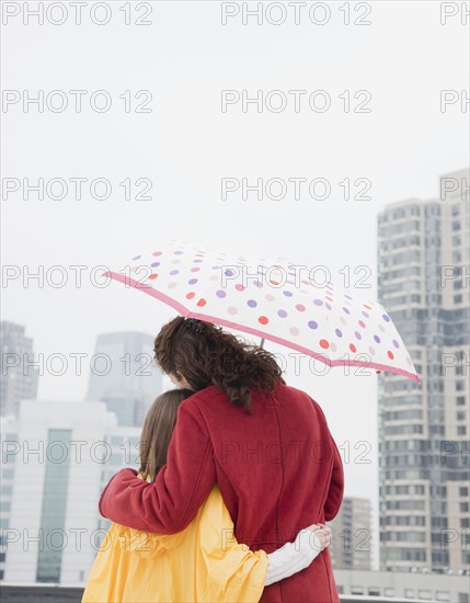 USA, New York City, mother and daughter (10-12 years) embracing under umbrella, rear view, Jersey City, New Jersey. Photographe : Jamie Grill