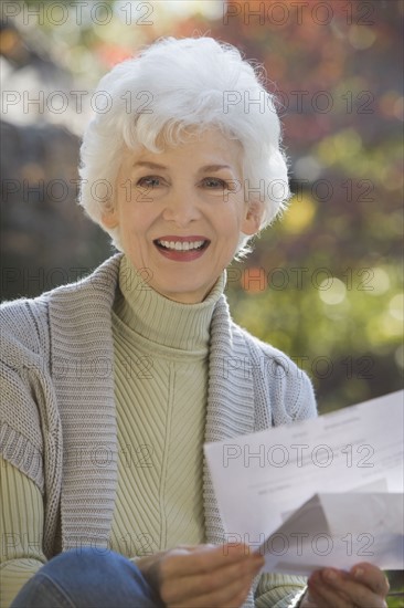 Portrait of senior woman holding mail outdoors. Photographe : mark edward atkinson