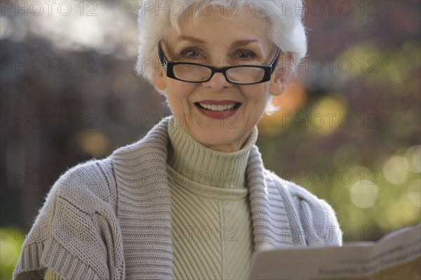 Portrait of senior woman reading newspaper outdoors. Photographe : mark edward atkinson