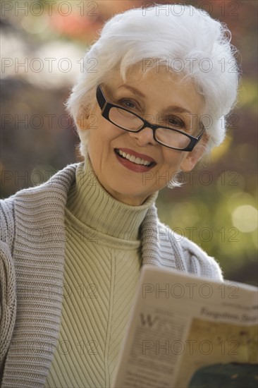 Portrait of senior woman reading newspaper outdoors. Photographe : mark edward atkinson