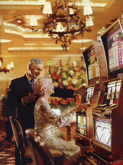 Senior couple in casino playing on slot machines, Las Vegas, Nevada, USA. Photographe : Stewart Cohen