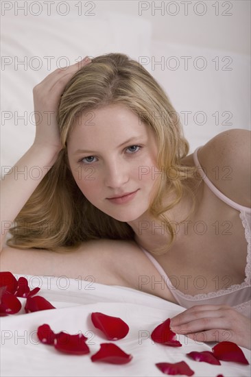 Young woman laying in bed with flower pedals. Photographe : David Engelhardt