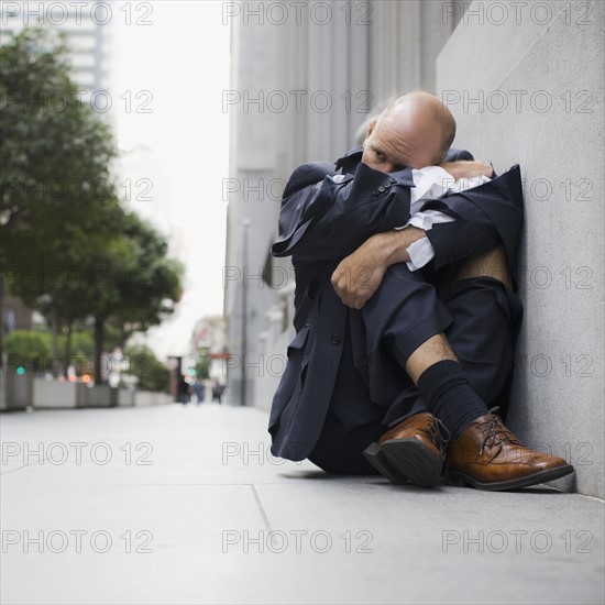 Businessman wearing torn clothing, sitting on sidewalk, San Francisco, California, USA. Photographe : PT Images
