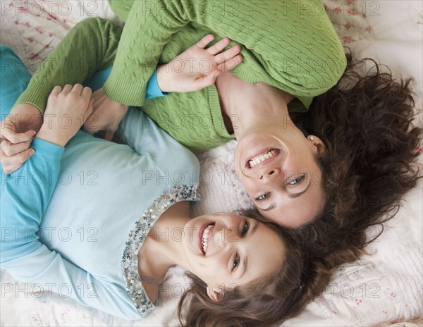 Mother and daughter (10-12 years) lying on bed, smiling, portrait, directly above. Photographe : Jamie Grill