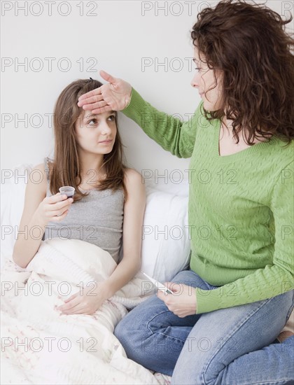 Mother measuring daughter's (10-12 years) fever. Photographe : Jamie Grill