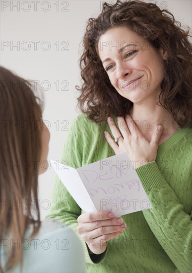 Mother receiving greeting card on mother's day from daughter (10-12 years). Photographe : Jamie Grill