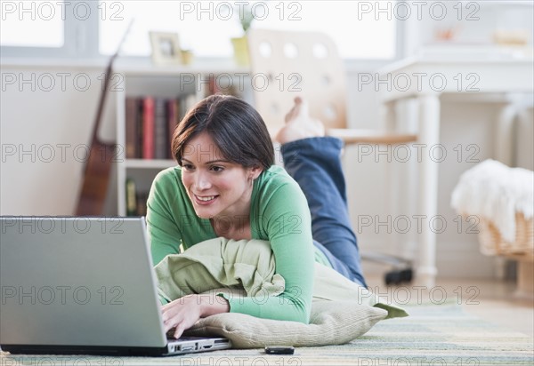 Mid-adult woman lying on floor using laptop.