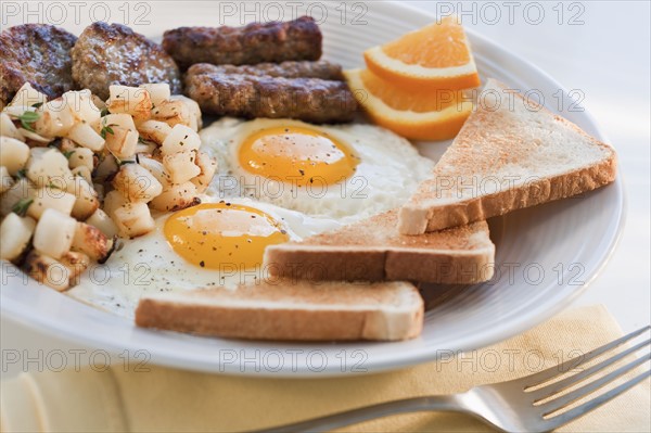 Fried sausages on plate with eggs and plates in background.