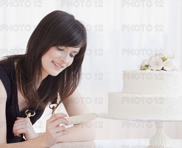 Young woman observing wedding cake, studio shot. Photographe : Jamie Grill