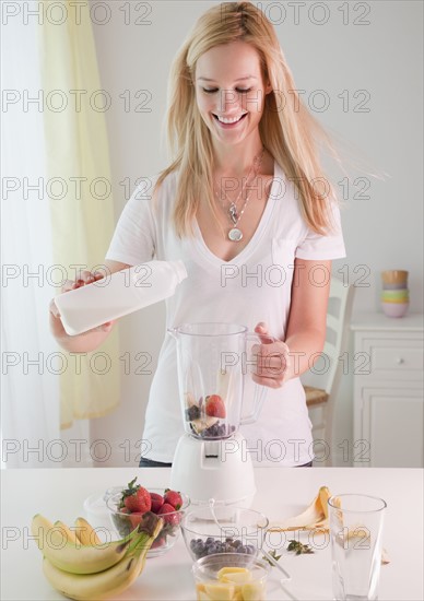 Young woman preparing fruit milkshake in liquidizer. Photographe : Jamie Grill