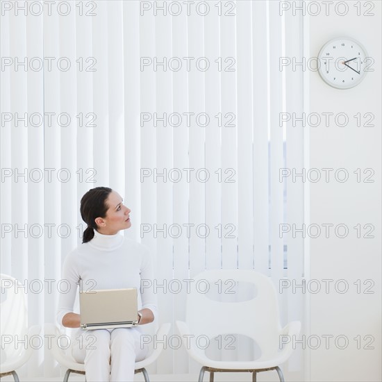 Businesswoman looking at clock in waiting room.