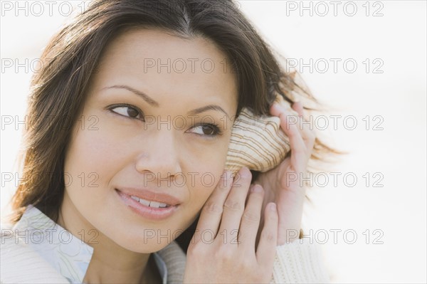 Close-up of woman listening to shell. Photographe : PT Images