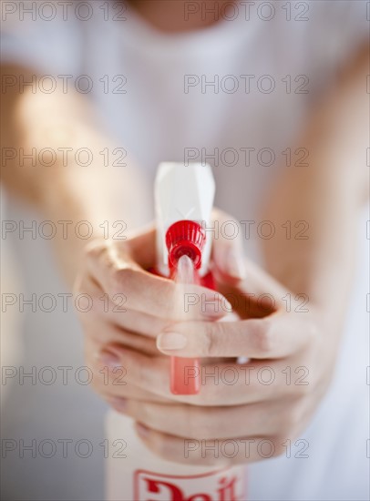 Woman holding and spraying cleaning fluid, close-up.