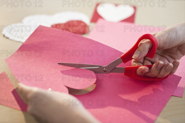 Woman cutting out heart in paper, close-up.