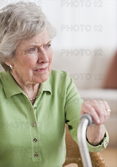 Senior woman sitting and holding walking stick.