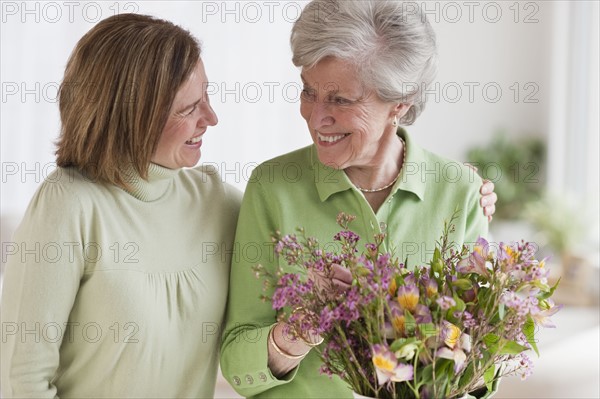 Daughter hugging mother holding flowers.