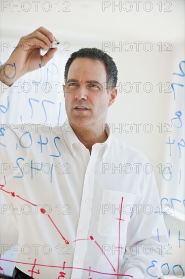 Mature businessman writing numbers on transparent glass wall.