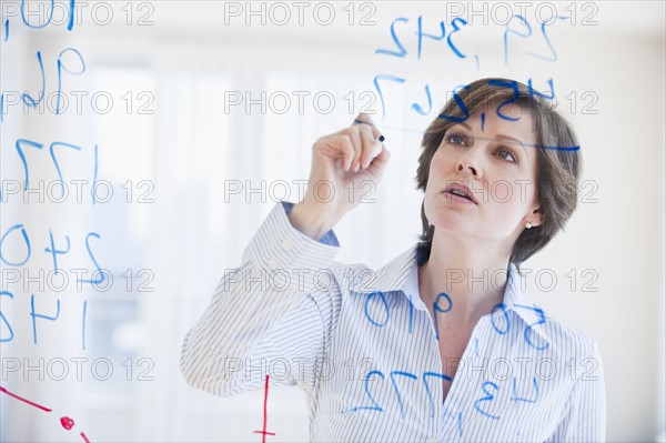 Mature businesswoman writing numbers on transparent glass wall.