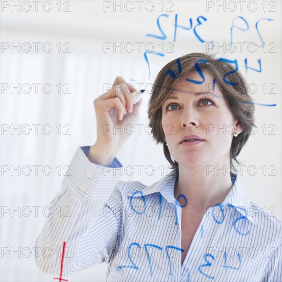 Mature businesswoman writing numbers on transparent glass wall.