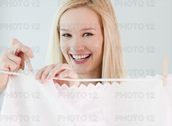 Portrait of young woman hanging laundry on washing line. Photographe : Jamie Grill