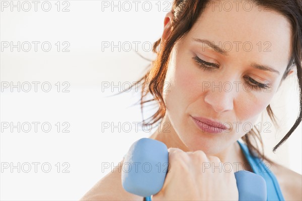 Woman using dumbbell, studio shot. Photographe : Daniel Grill