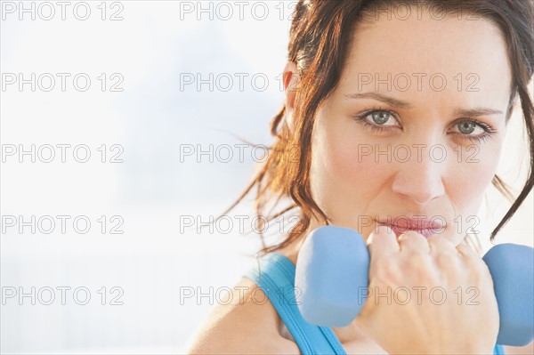 Studio portrait of woman using dumbbell. Photographe : Daniel Grill